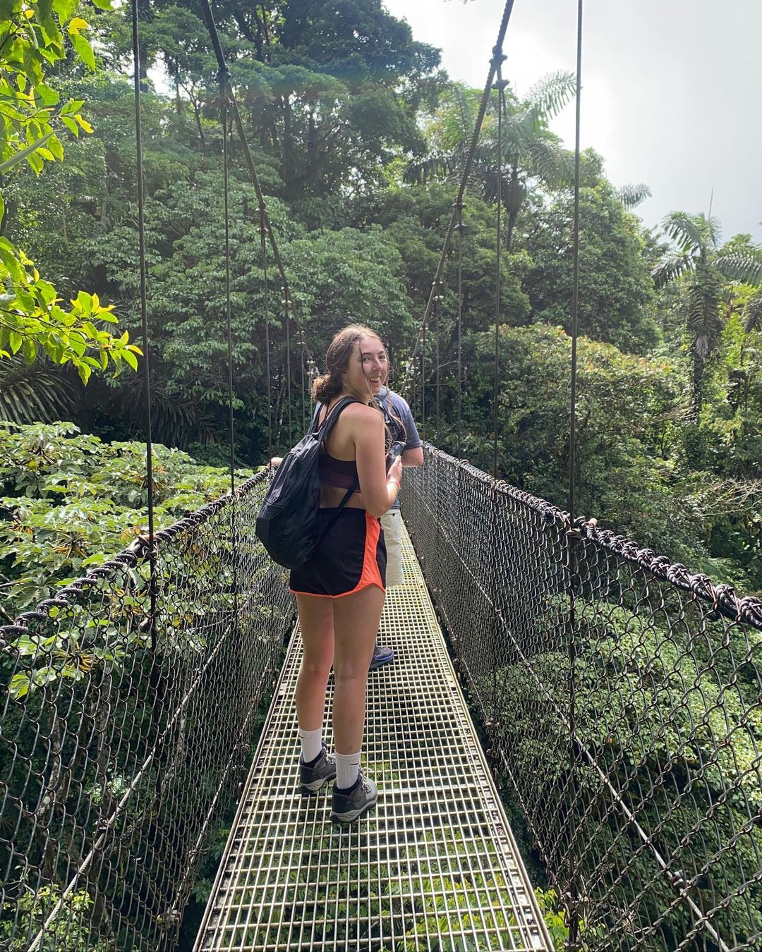 Girl walking on metal bridge above trees